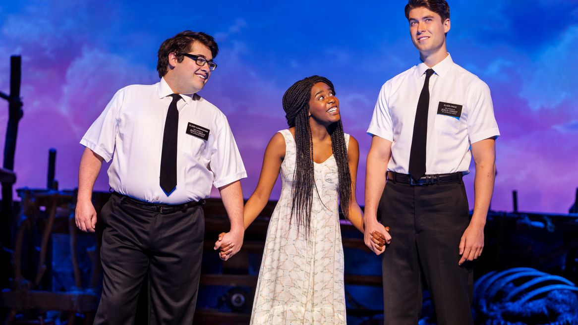 two young men in Mormon missionary clothing hold hands with a young woman 