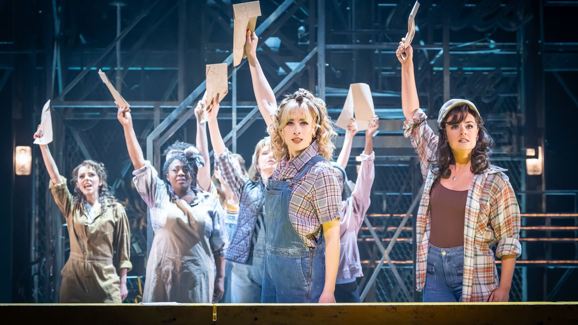 A group of determined looking woman stand with their arms in the air holding papers