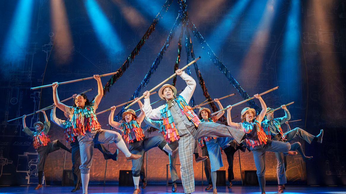 A group of people in colourful waistcoats dance with long sticks of bamboo