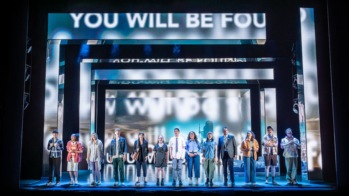 A group of young people stand in a line singing in front of the words 'You Will Be Found'