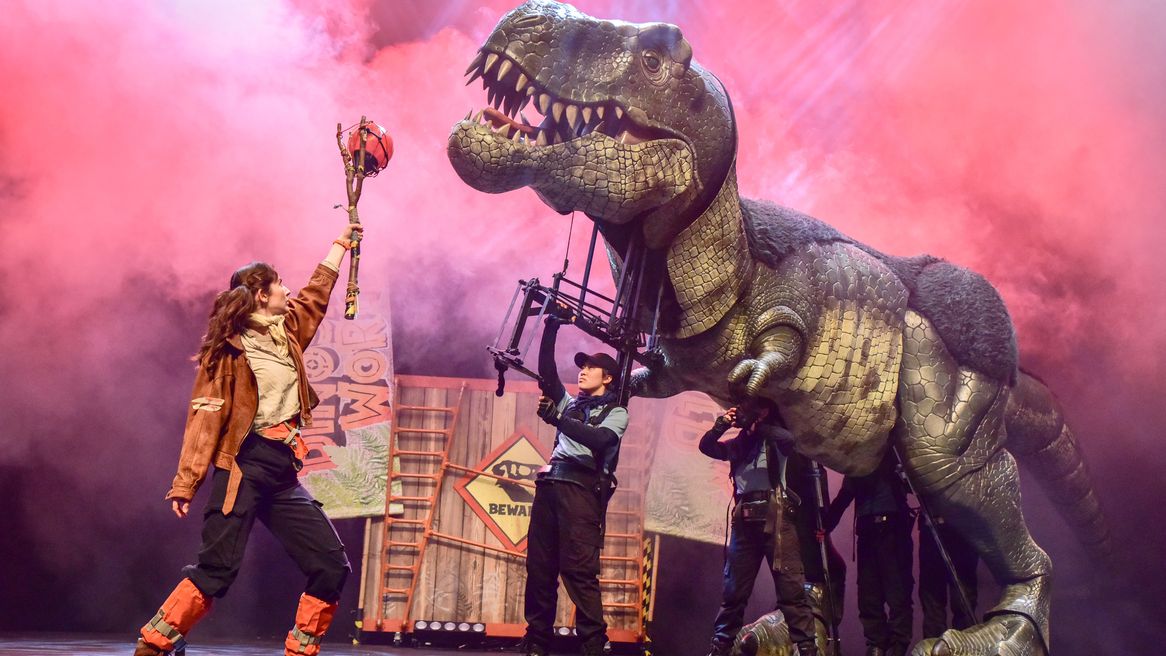 A woman offers food to a large Tyrannosaurus Rex puppet