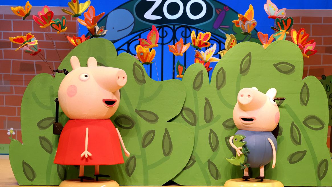 Animated pig characters in front of a zoo with green bushes behind them 