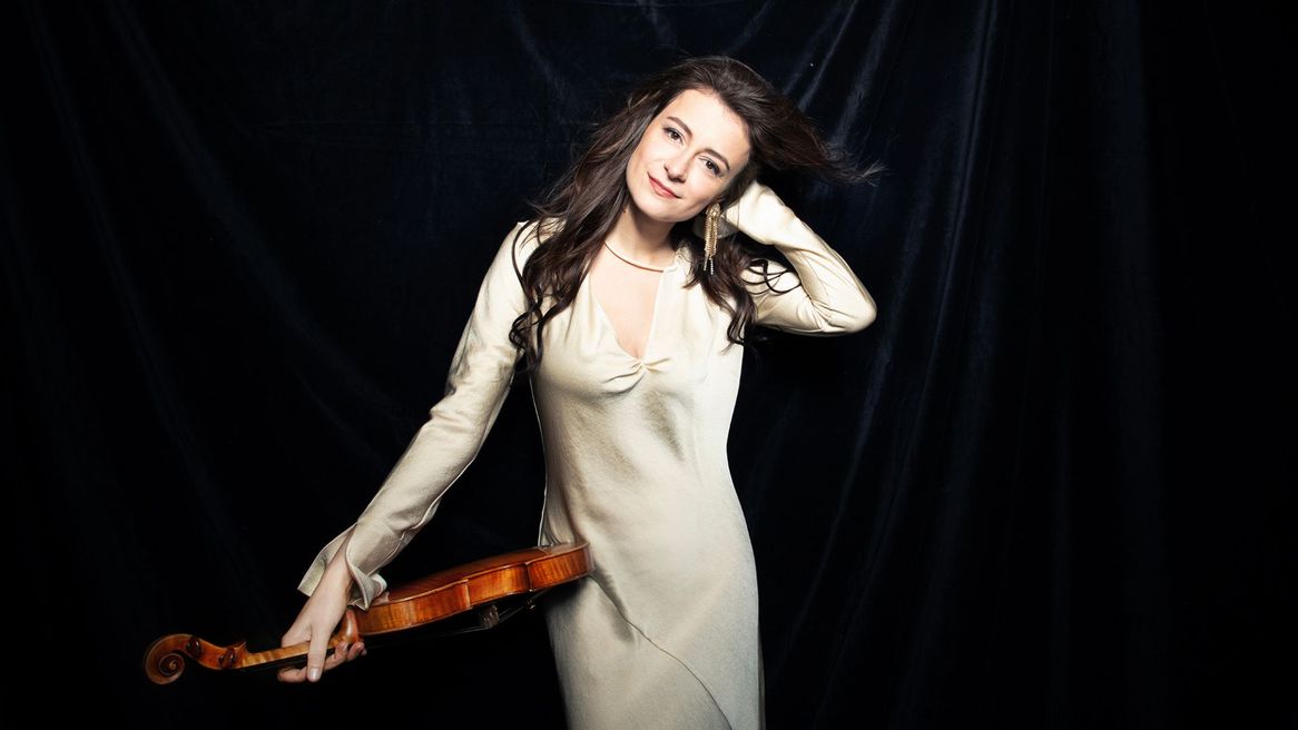 Violinist in a cream coloured dress with a black background 