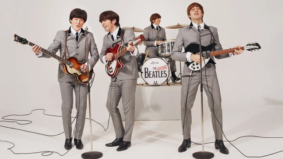 Four men perform as the Beatles with grey suits and bowl cuts.